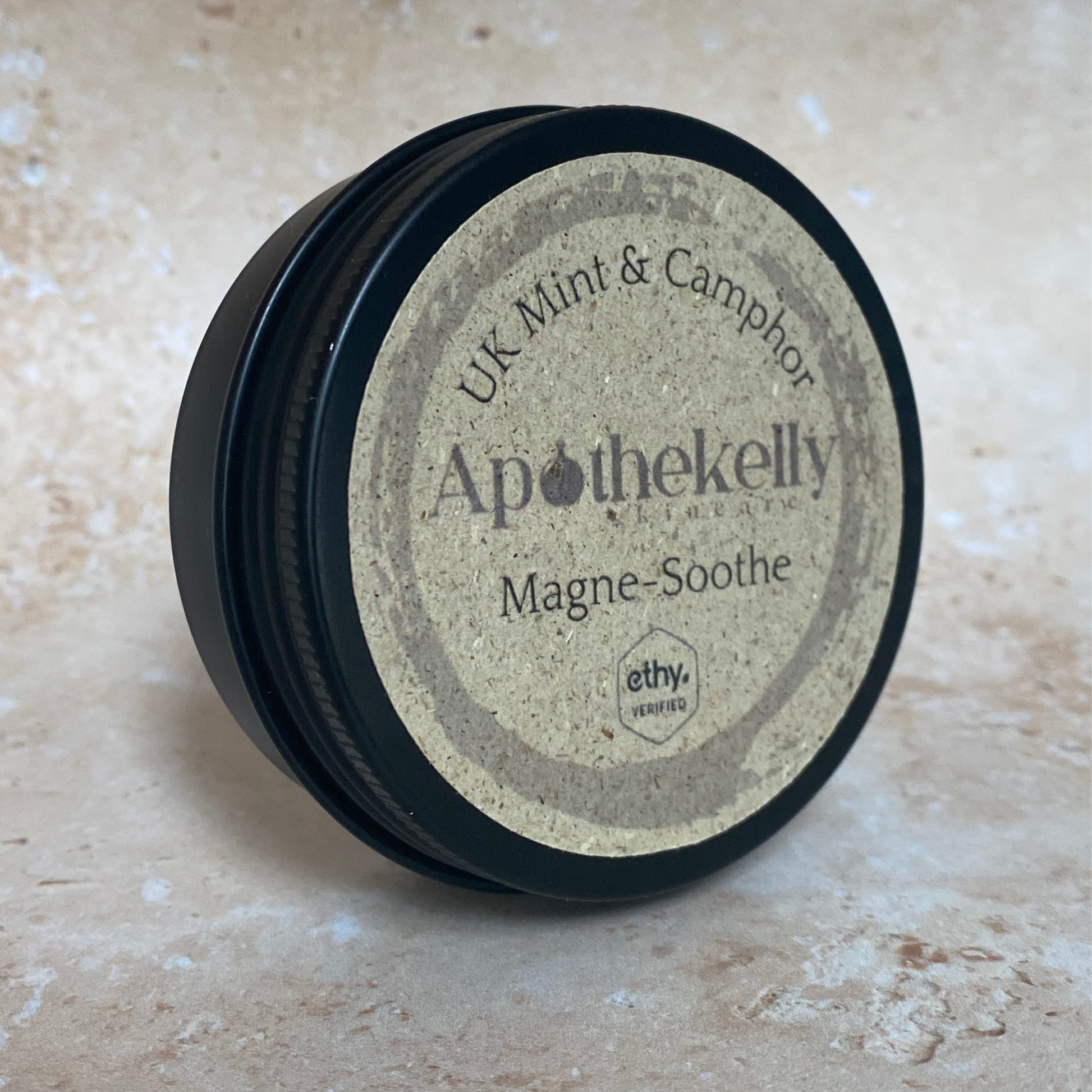 Apothekelly Magne-Soothe tin on a beige surface